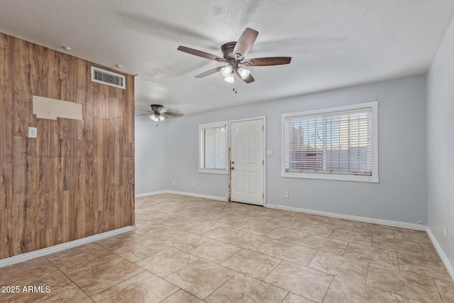 unfurnished room featuring ceiling fan, light tile patterned floors, wood walls, and a textured ceiling