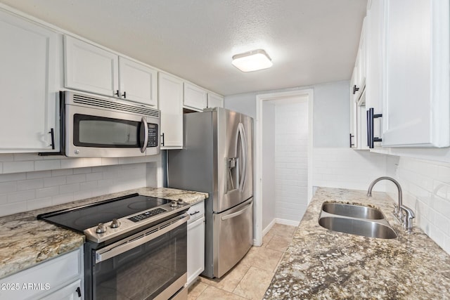 kitchen with a textured ceiling, appliances with stainless steel finishes, white cabinetry, sink, and light stone counters