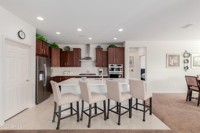 kitchen featuring wall chimney range hood, sink, a breakfast bar, stainless steel appliances, and an island with sink