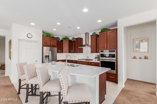 kitchen with appliances with stainless steel finishes, an island with sink, sink, a kitchen breakfast bar, and wall chimney range hood