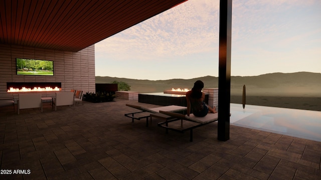 patio terrace at dusk with a fireplace and a water and mountain view