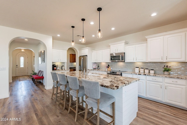 kitchen with hanging light fixtures, stainless steel appliances, an island with sink, and white cabinets