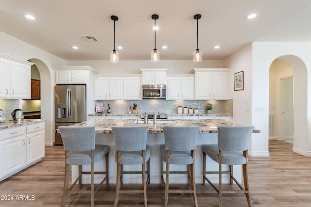 kitchen featuring white cabinetry, stainless steel appliances, light stone counters, and a center island with sink