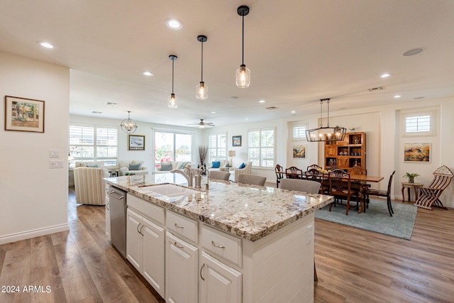 kitchen with dishwasher, an island with sink, sink, white cabinetry, and light hardwood / wood-style flooring