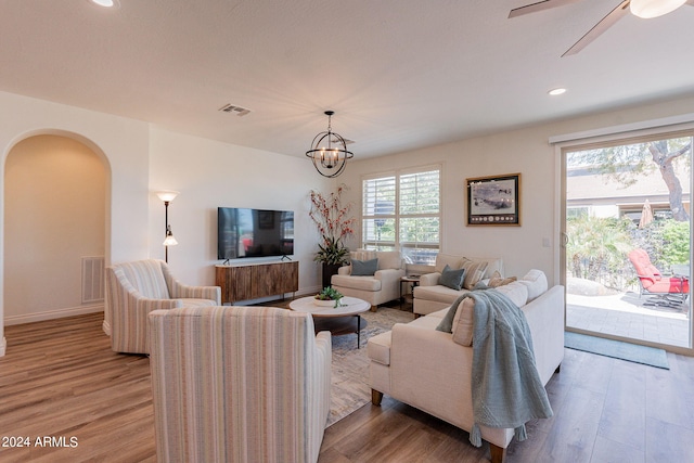 living room with ceiling fan with notable chandelier and light hardwood / wood-style flooring