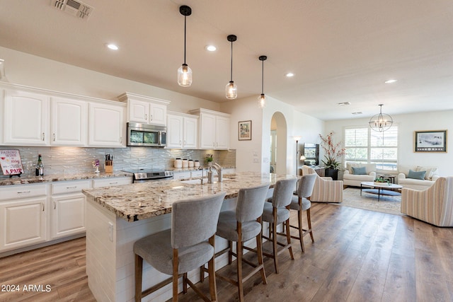 kitchen with white cabinetry, light stone counters, a kitchen island with sink, and stainless steel appliances