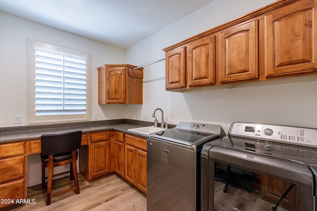 clothes washing area with sink, light hardwood / wood-style flooring, cabinets, and washing machine and clothes dryer