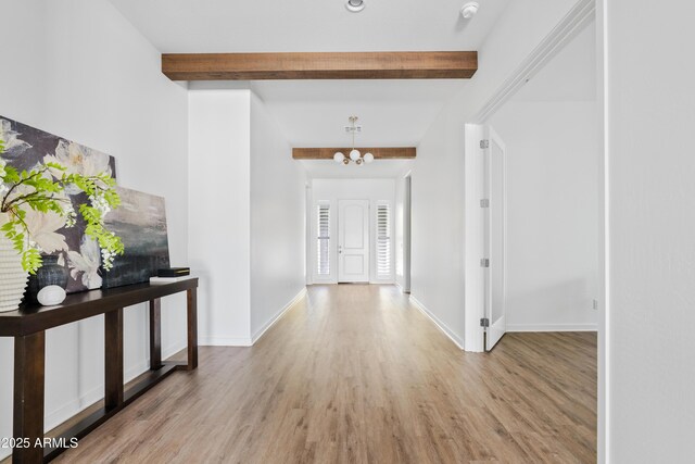 hallway featuring baseboards, beamed ceiling, wood finished floors, and a chandelier