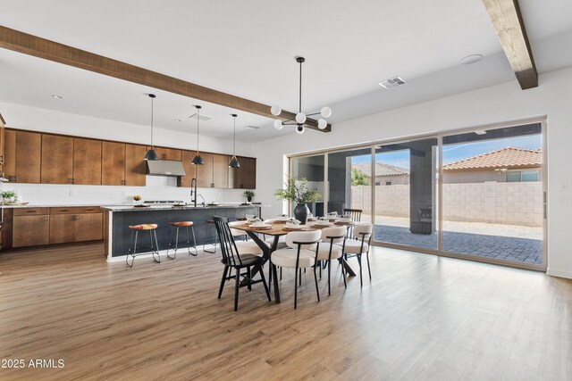 dining space featuring beamed ceiling, light wood finished floors, a chandelier, and visible vents