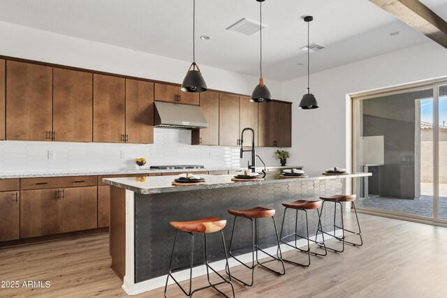 kitchen with under cabinet range hood, decorative backsplash, a kitchen bar, and light wood-type flooring