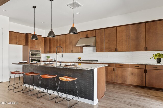 kitchen with under cabinet range hood, appliances with stainless steel finishes, light wood-style flooring, and a breakfast bar area