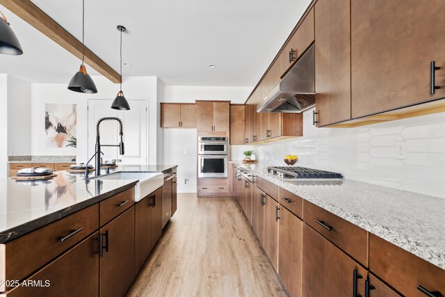 kitchen featuring a sink, light stone countertops, under cabinet range hood, and light wood-style flooring