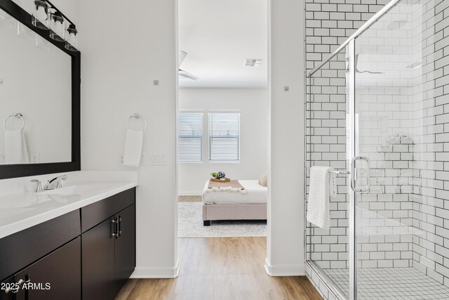 ensuite bathroom featuring baseboards, a shower stall, wood finished floors, and vanity