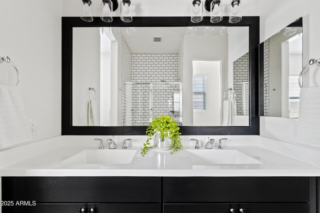 full bath featuring double vanity, tiled shower, and a sink