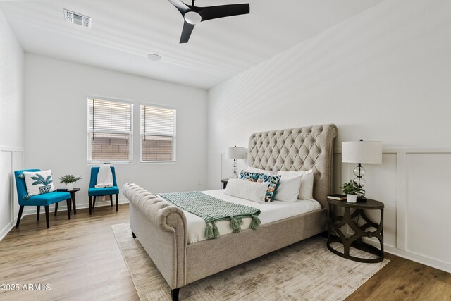 bedroom with visible vents, ceiling fan, a wainscoted wall, and light wood-type flooring