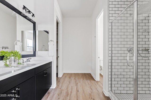 full bathroom featuring double vanity, a stall shower, wood finished floors, a sink, and baseboards