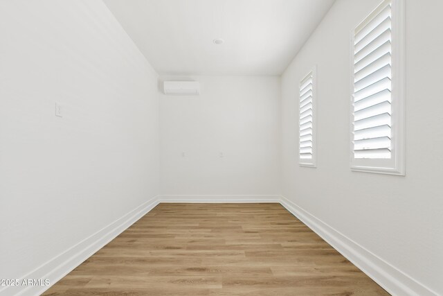 empty room featuring an AC wall unit, baseboards, and light wood-type flooring