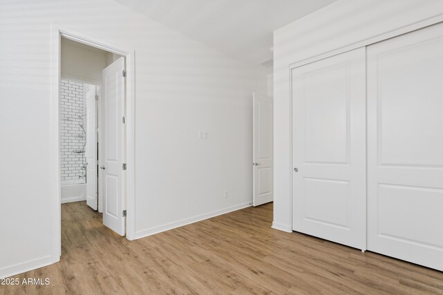 unfurnished bedroom with light wood-type flooring, baseboards, lofted ceiling, and a closet