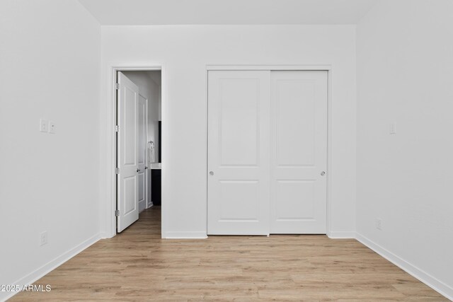 unfurnished bedroom featuring light wood-style floors, baseboards, and a closet