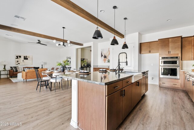 kitchen with visible vents, a sink, beamed ceiling, light wood-style floors, and stainless steel appliances