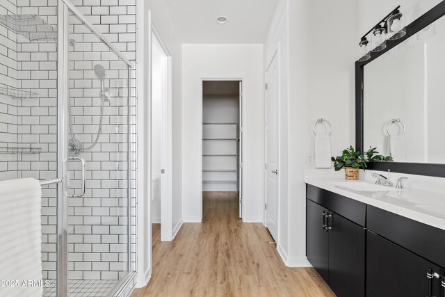 full bathroom with a walk in closet, vanity, baseboards, a shower stall, and wood finished floors