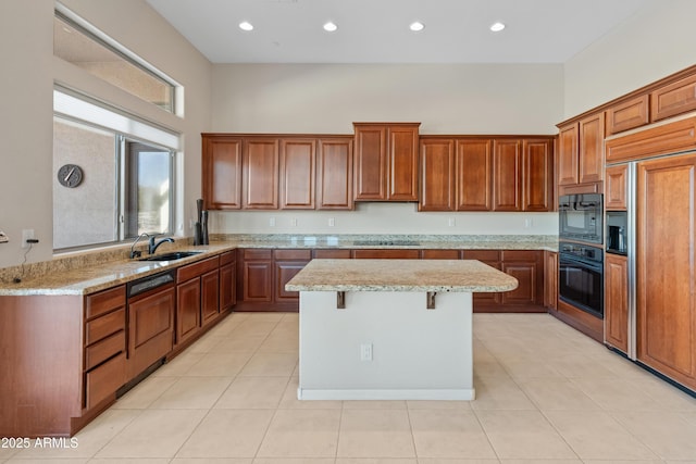 kitchen featuring light stone counters, a center island, black appliances, and sink