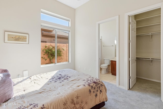 bedroom featuring connected bathroom, a walk in closet, a closet, and light colored carpet