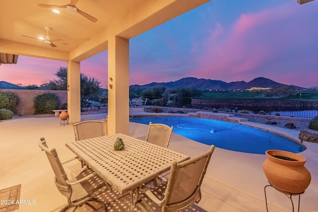 pool at dusk with a mountain view, a patio, and ceiling fan