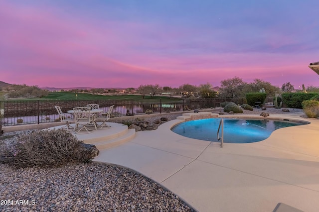 pool at dusk with a water view and a patio