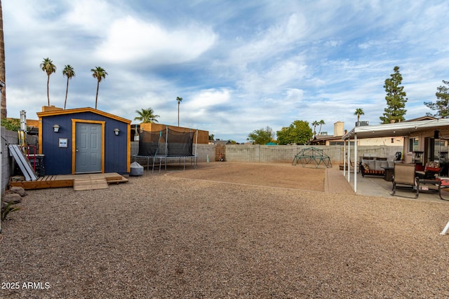 view of yard with an outbuilding, a patio, a fenced backyard, a storage unit, and a trampoline