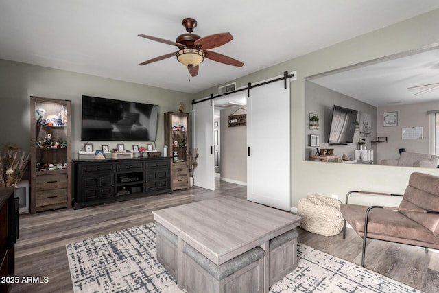 living room featuring a barn door, wood finished floors, visible vents, a ceiling fan, and baseboards