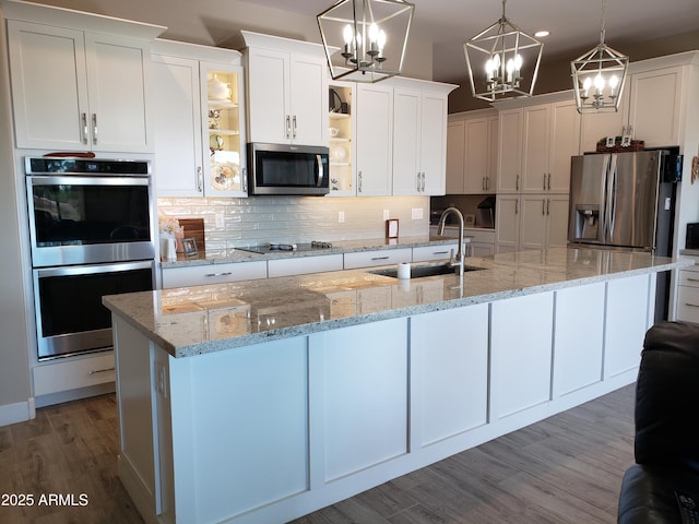 kitchen featuring a kitchen island with sink, stainless steel appliances, decorative light fixtures, and white cabinets