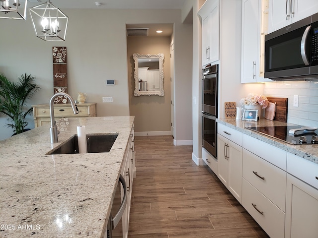 kitchen with pendant lighting, stainless steel appliances, white cabinetry, a sink, and light stone countertops