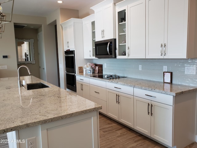 kitchen featuring glass insert cabinets, white cabinets, a sink, and black appliances