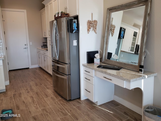 kitchen with light stone counters, wood finish floors, white cabinetry, stainless steel fridge, and glass insert cabinets