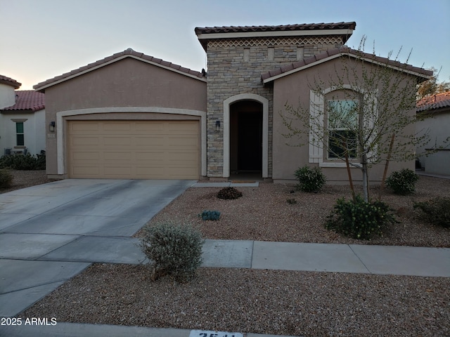 mediterranean / spanish-style house with a tile roof, stucco siding, an attached garage, stone siding, and driveway