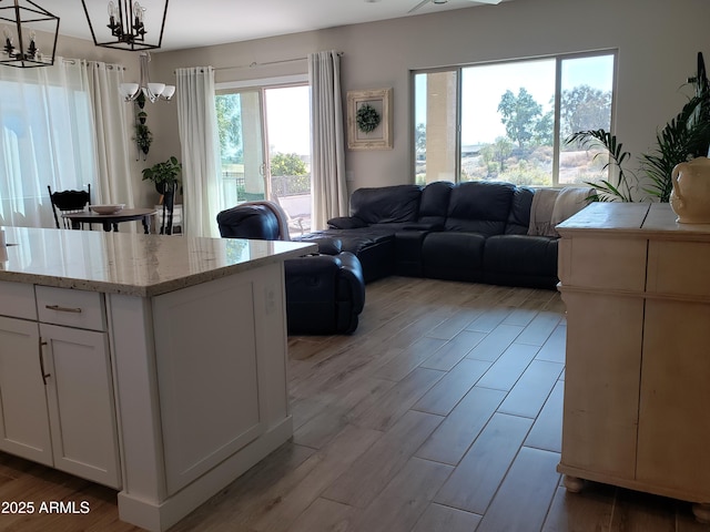 interior space featuring light stone counters, light wood-style flooring, white cabinetry, open floor plan, and decorative light fixtures