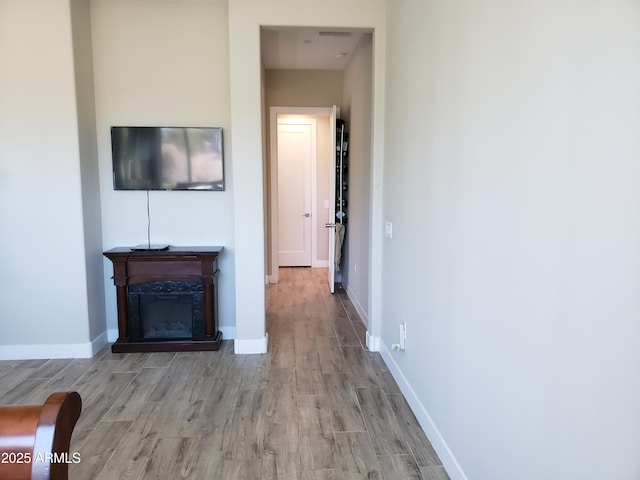 unfurnished living room with a glass covered fireplace, light wood-style flooring, and baseboards