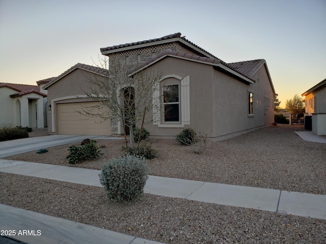 mediterranean / spanish house with a garage, driveway, a tile roof, and stucco siding