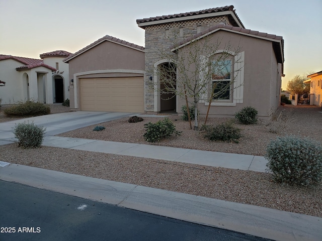 mediterranean / spanish home with stucco siding, concrete driveway, a garage, stone siding, and a tiled roof