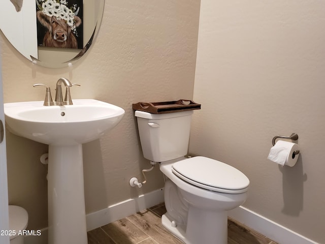 half bath with baseboards, a textured wall, toilet, and wood finished floors