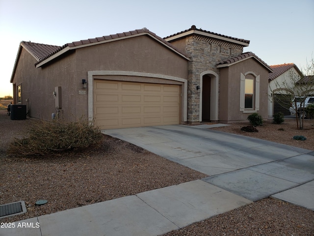 mediterranean / spanish home featuring central air condition unit, a garage, stone siding, concrete driveway, and stucco siding