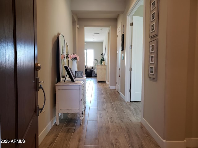 hallway featuring light wood-style flooring and baseboards