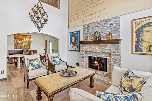 living room featuring a notable chandelier, a stone fireplace, and a high ceiling