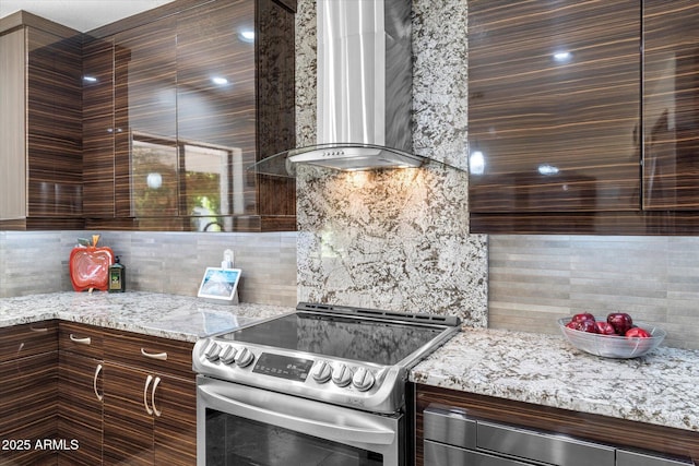 kitchen with electric stove, wall chimney range hood, light stone counters, tasteful backsplash, and dark brown cabinetry