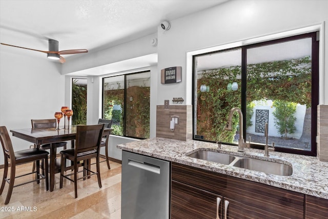 kitchen with dark brown cabinetry, sink, stainless steel dishwasher, ceiling fan, and light stone countertops