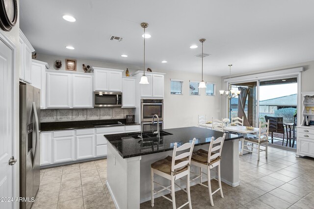 kitchen featuring an island with sink, sink, decorative light fixtures, white cabinetry, and appliances with stainless steel finishes