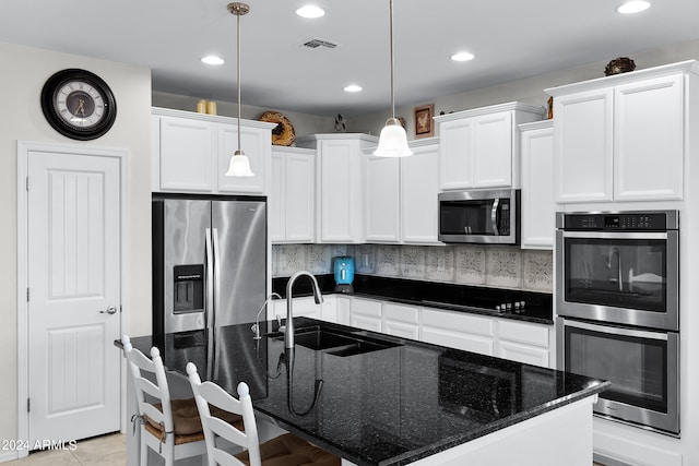 kitchen featuring pendant lighting, an island with sink, stainless steel appliances, and dark stone counters