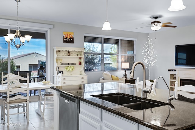 kitchen featuring hanging light fixtures, dark stone counters, sink, light tile patterned floors, and white cabinetry