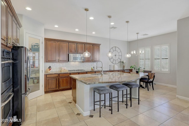 kitchen featuring pendant lighting, sink, light stone counters, a kitchen island with sink, and stainless steel appliances